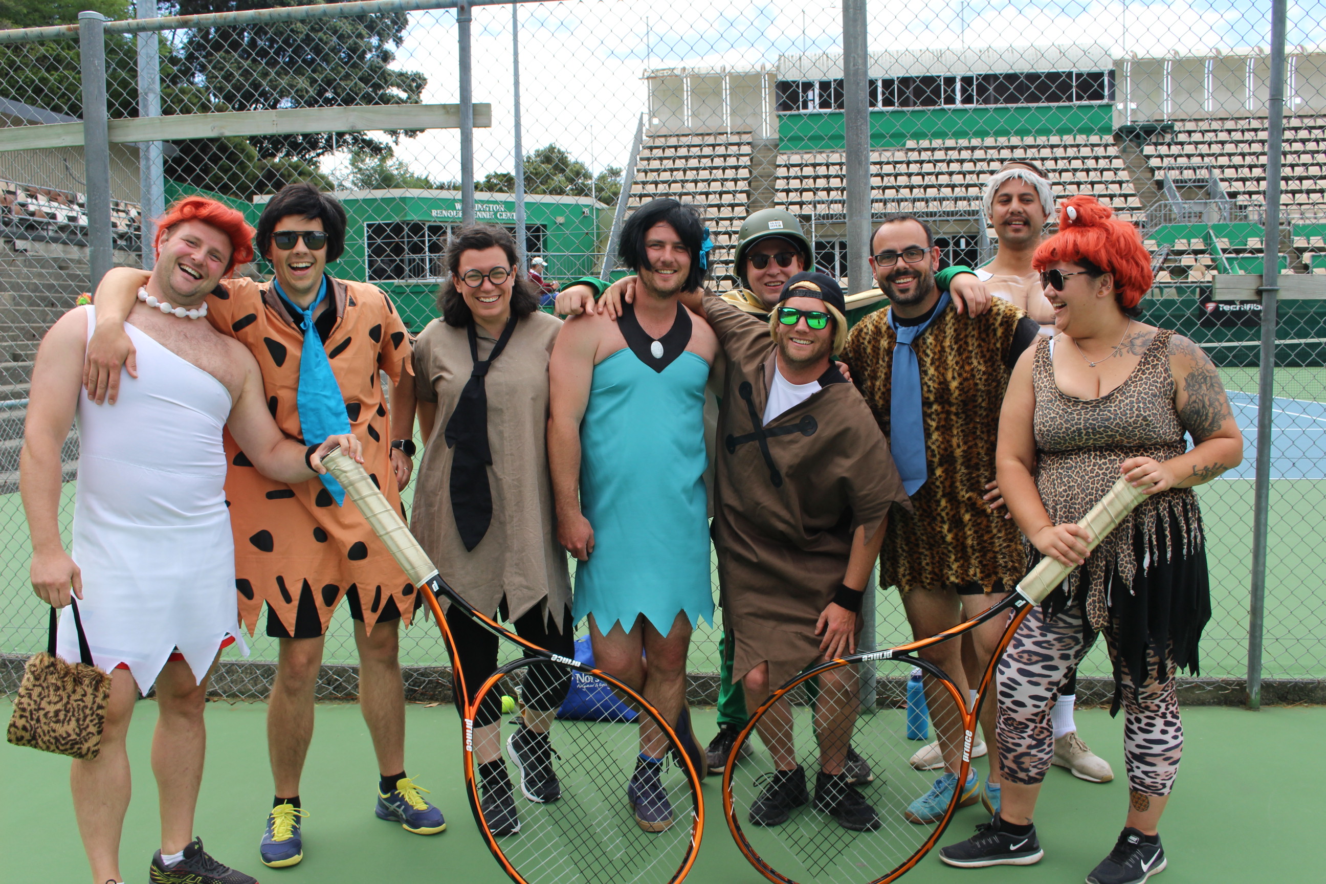 Corporate team in Flintston costumes holding jumbo sized tennis rackets.