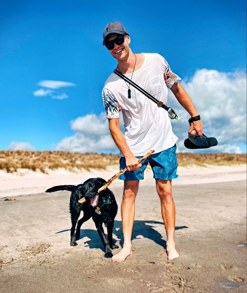 James, a young adult and cancer sufferer, at the beach on a summer's day with his black lab.