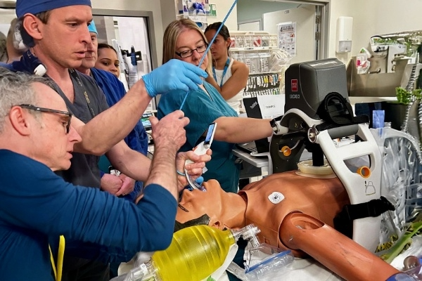 doctors in blue scrubs training with medical manikin.