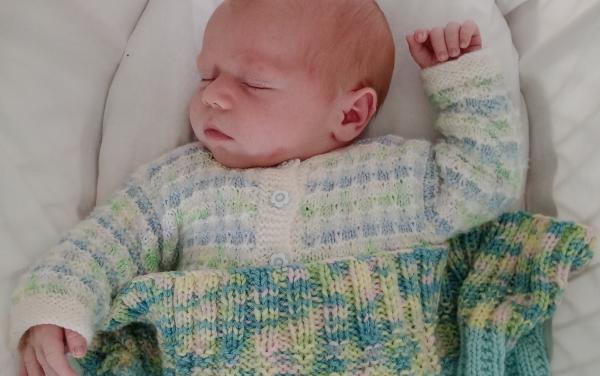 Baby sleeping in basinet wearing knitted jacket and wrapped in knitted blanket