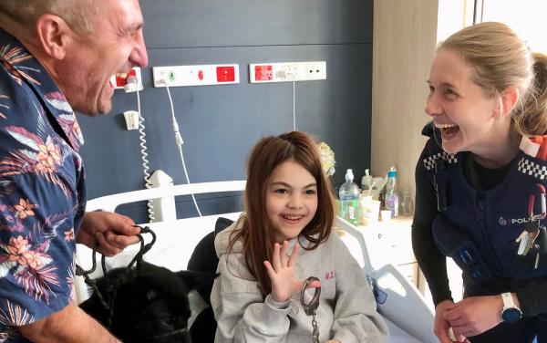 Police officers share a laugh with a young patient holding handcuffs.