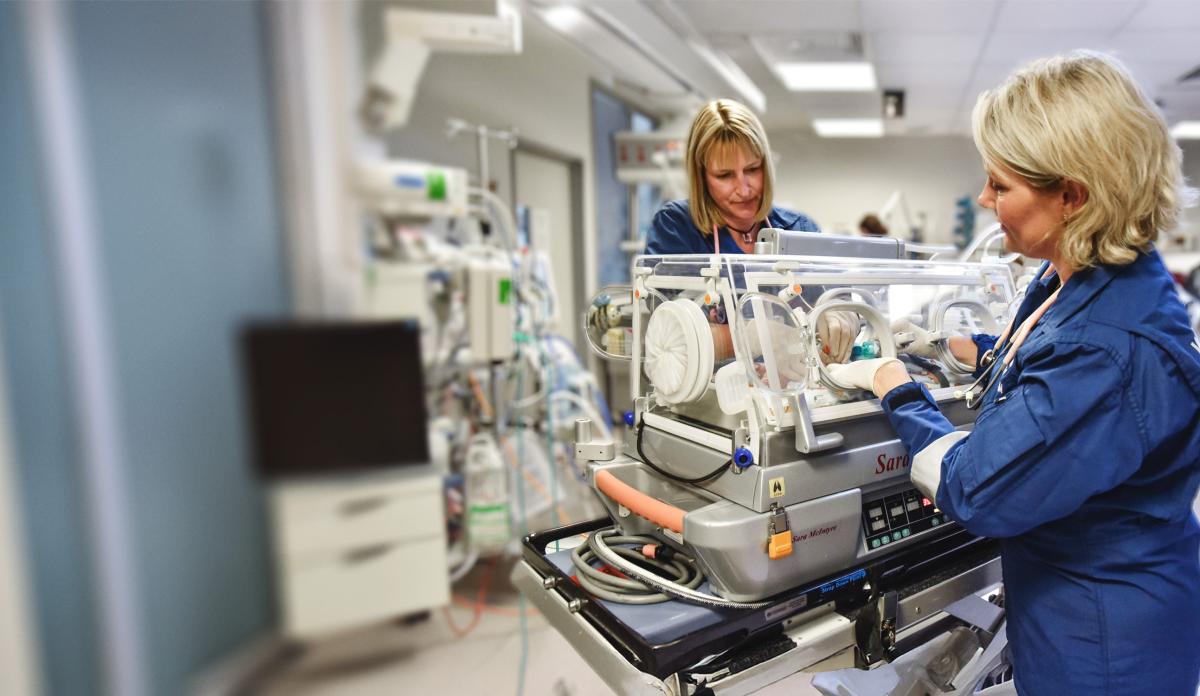 Two NICU flight retrieval doctors care for a premature baby in a mobile intensive care incubator.