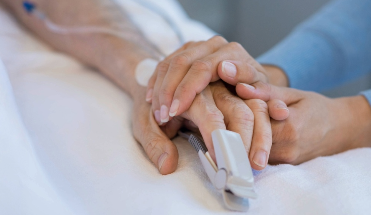 Volunteer holds a patient's hand, attached to a medical device.